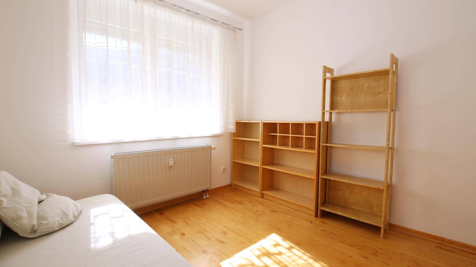 Schlafzimmer mit Parkettboden, viel Tageslicht und praktischen Holzregalen.