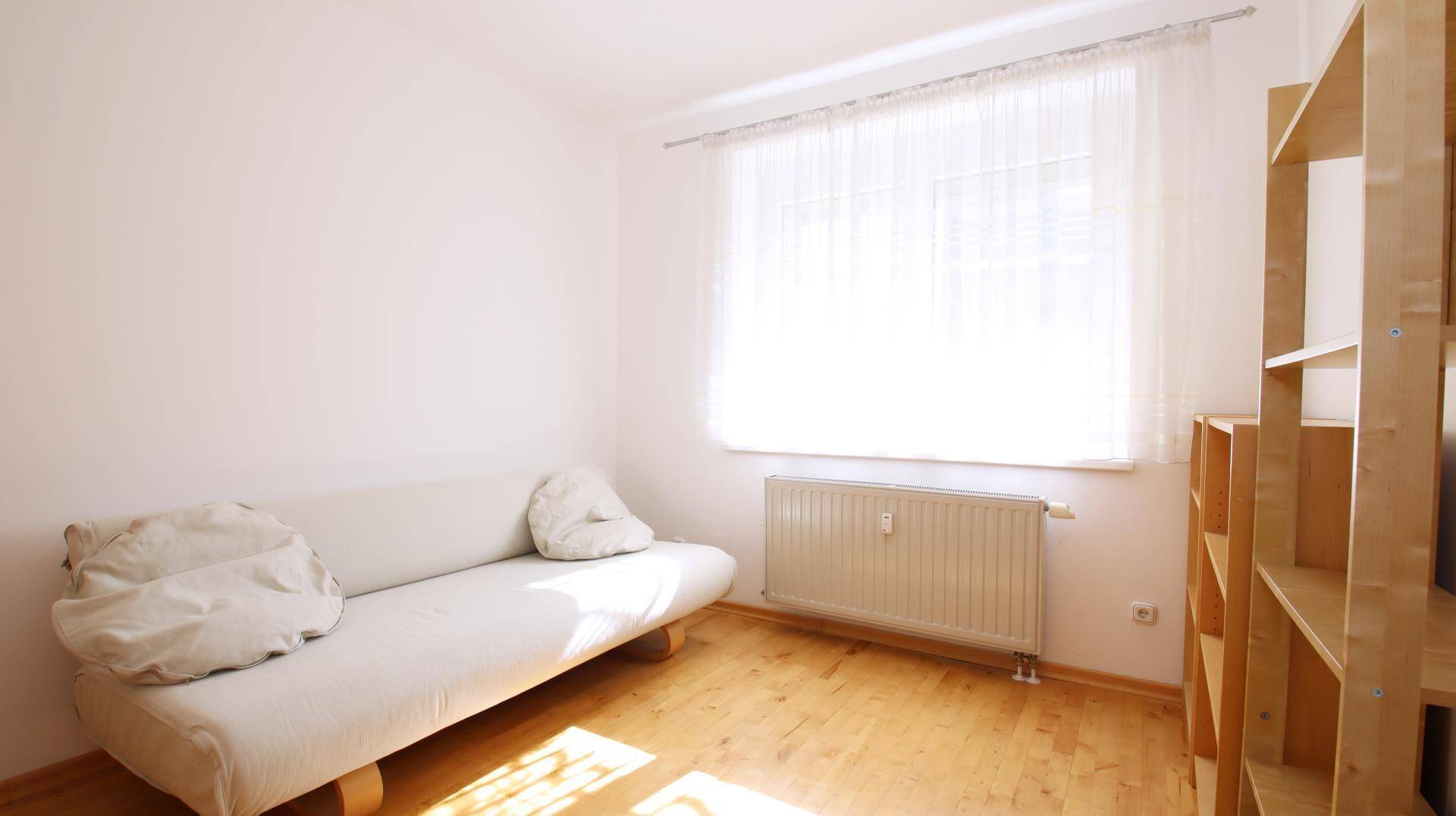 Helles Schlafzimmer mit Parkettboden, einem einfachen Sofa und großem Fenster.