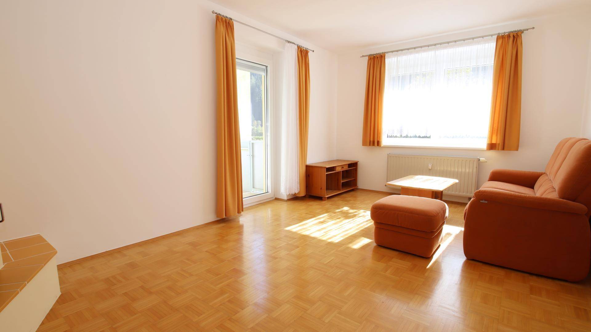 Gemütliches Wohnzimmer mit Parkettboden, Heizkörper und einem bequemen Sofa in warmen Farbtönen.
