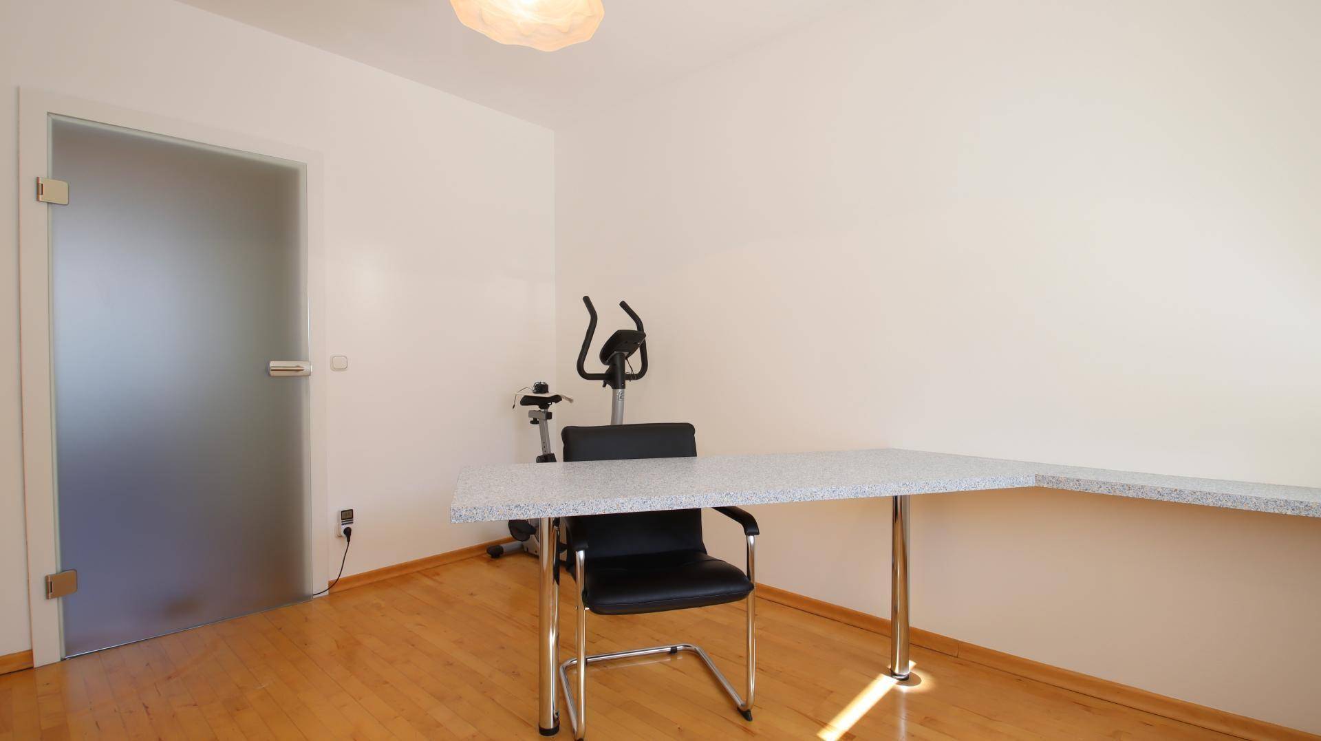 Arbeitszimmer mit Parkettboden, Schreibtisch und einem Heimtrainer, ideal für Home-Office und Fitness.