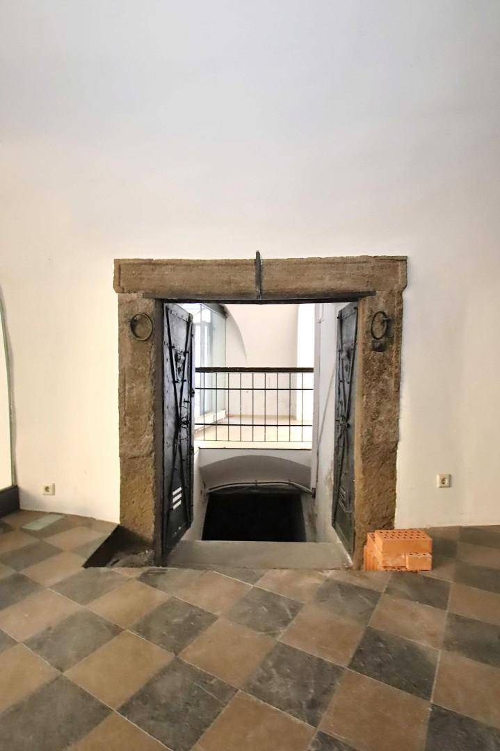 Historischer Steineingang mit schmiedeeisernen Toren, der zu einem tiefer gelegenen Bereich führt.