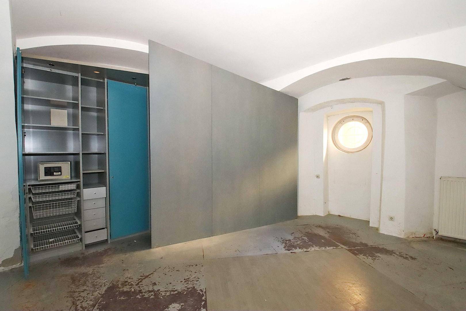 Lagerraum mit Gewölbedecken, einem modularen Schranksystem und einem markanten Rundfenster.