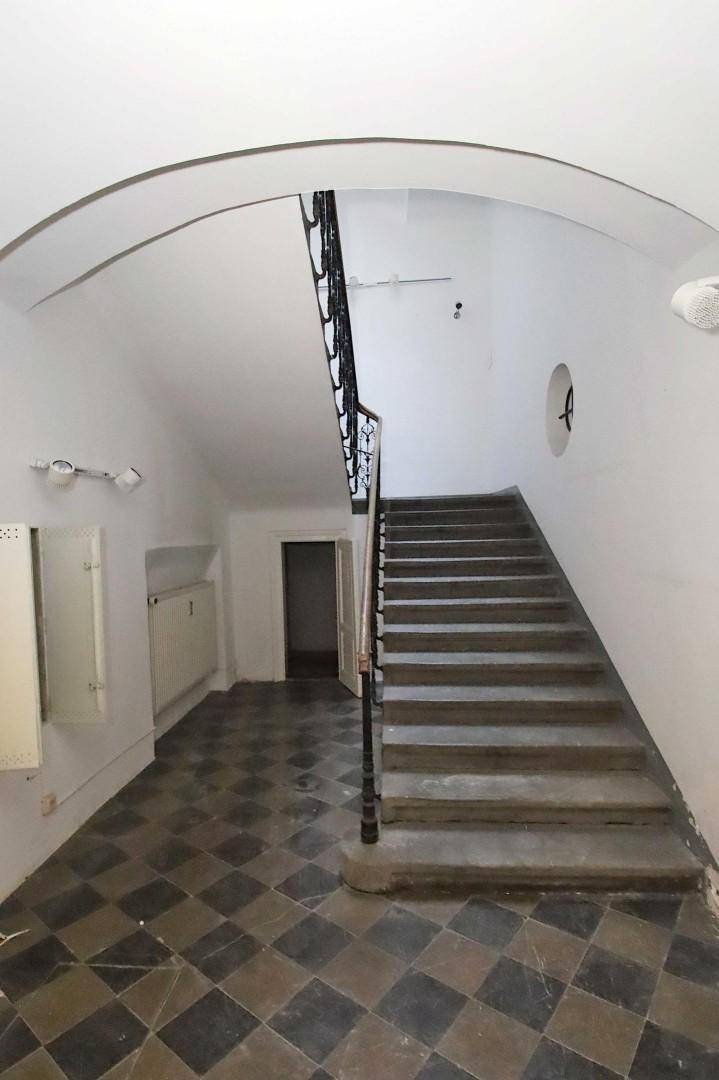 Historisches Treppenhaus mit schmiedeeisernem Geländer, Gewölbedecke und kariertem Fliesenboden.