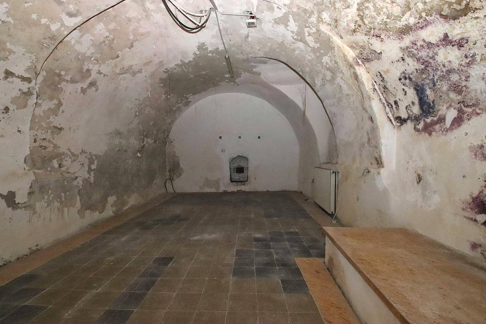 Alter Kellerraum mit Gewölbedecken, abblätternder Farbe und einem gefliesten Boden in schlechtem Zustand.