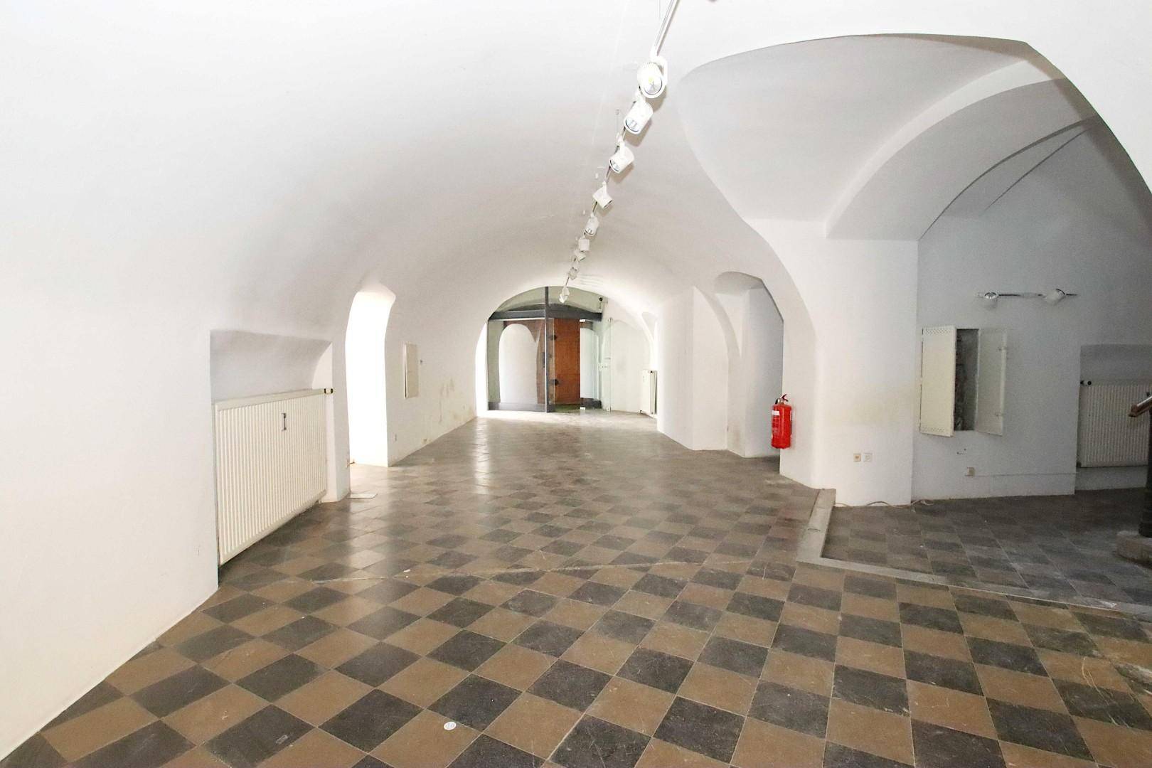 Kellerraum mit Gewölbedecken, kariertem Fliesenboden und Heizkörpern an den Wänden.