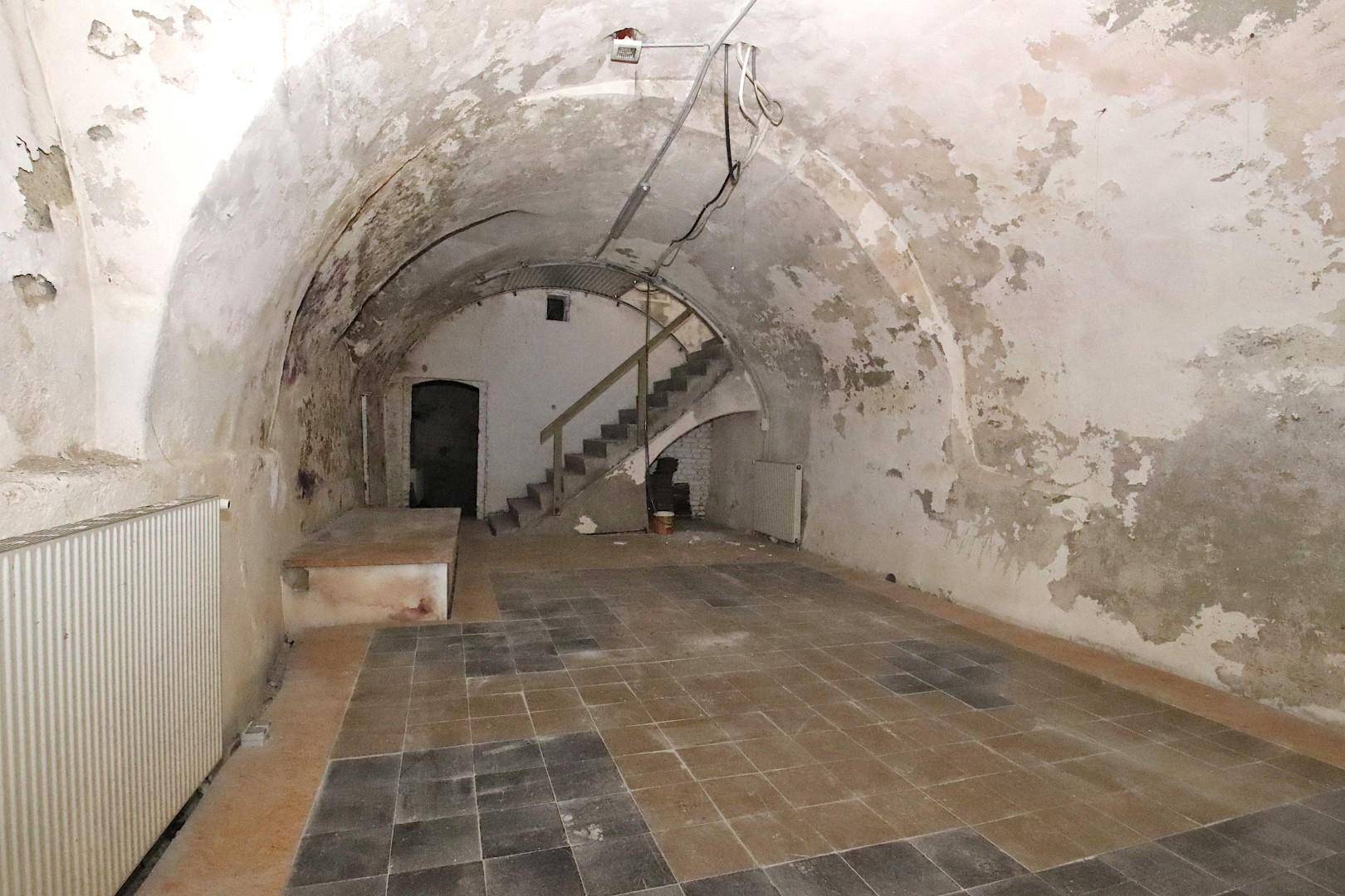 Geräumiger Kellerraum mit Gewölbedecken, sichtbaren Schäden an den Wänden und einer Treppe im Hintergrund.