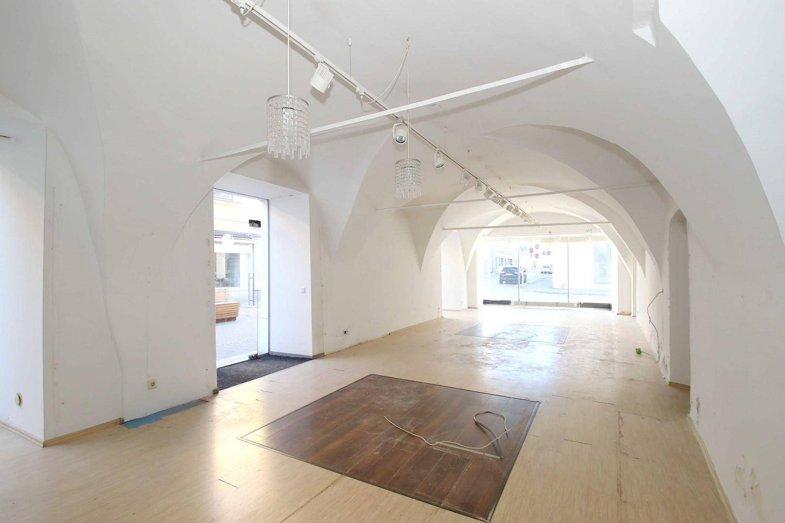 Heller Gewerberaum mit Gewölbedecken, Schaufenstern und dekorativen Kronleuchtern an der Decke.