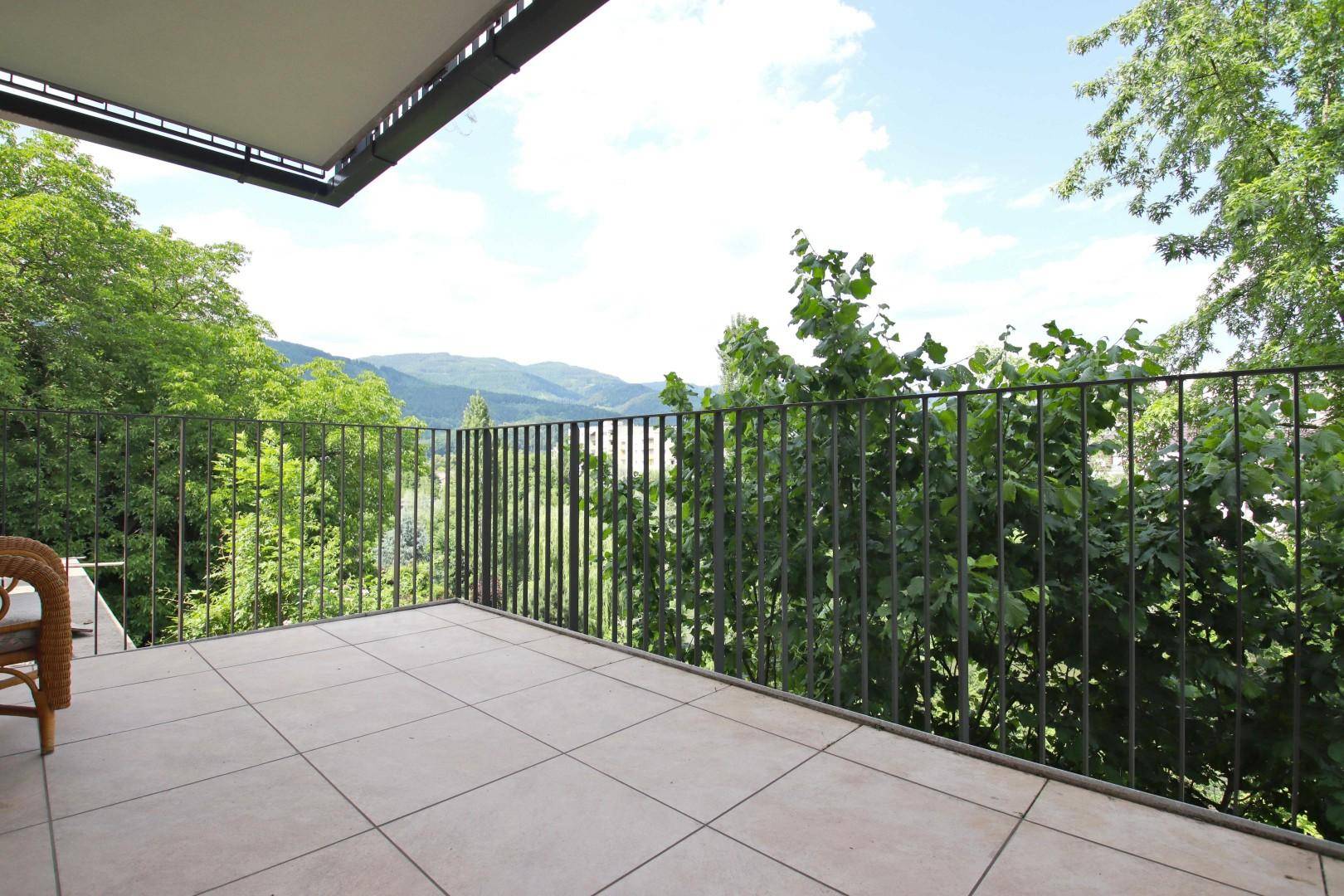 Großer Balkon mit Fliesenboden und weitem Blick auf die grüne Landschaft und Berge.