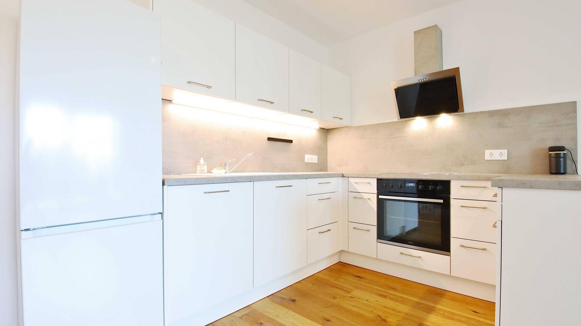 Moderne Einbauküche mit weißen Schränken, integrierten Geräten und Holzboden.