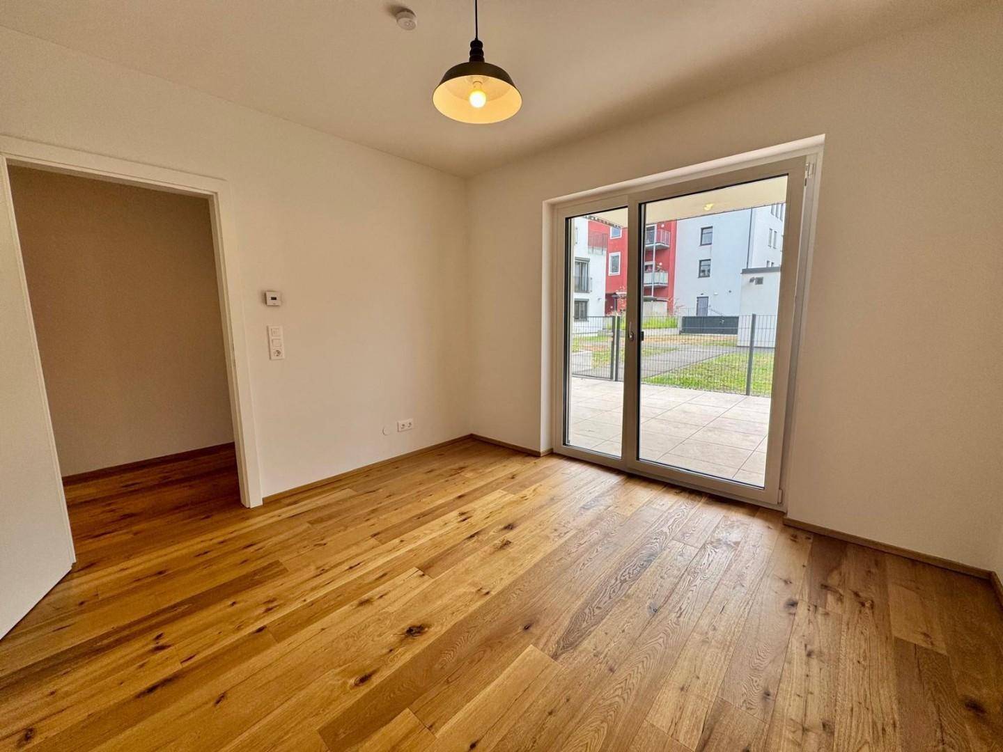 Leeres Zimmer mit Holzboden und großen Schiebetüren, die zu einem Außenbereich führen.