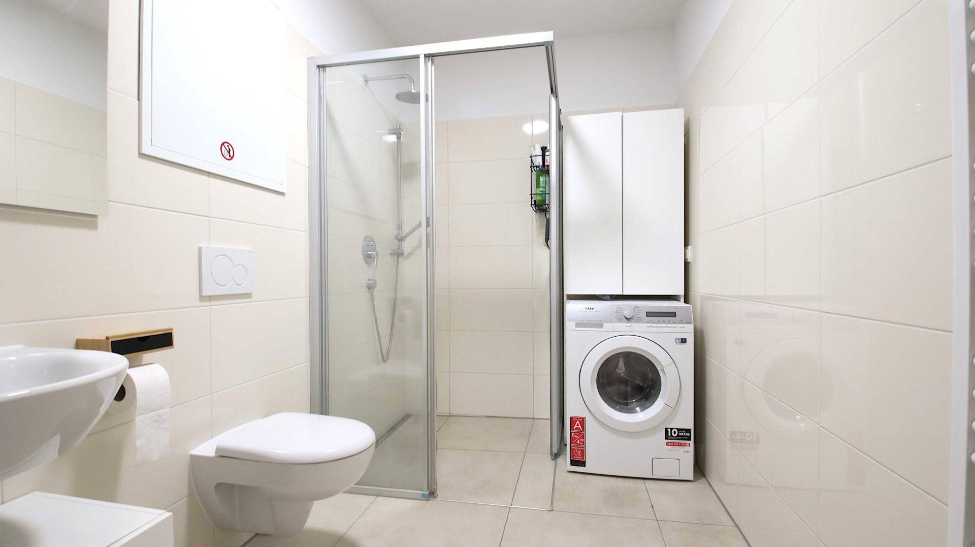 Modernes Badezimmer mit Duschkabine, WC, Waschbecken und Waschmaschine.
