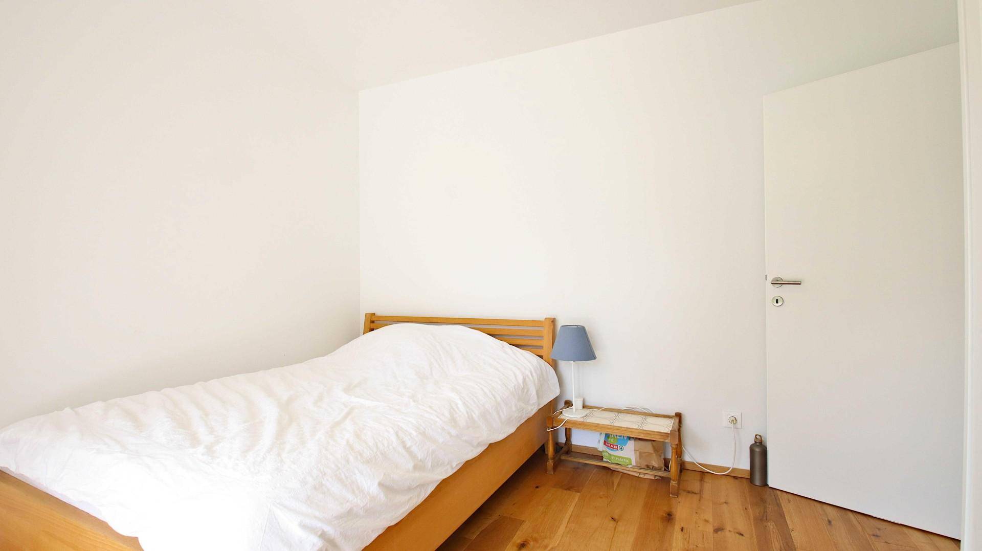 Einfaches Schlafzimmer mit Holzboden, weiß gestrichenen Wänden und einem Einzelbett.