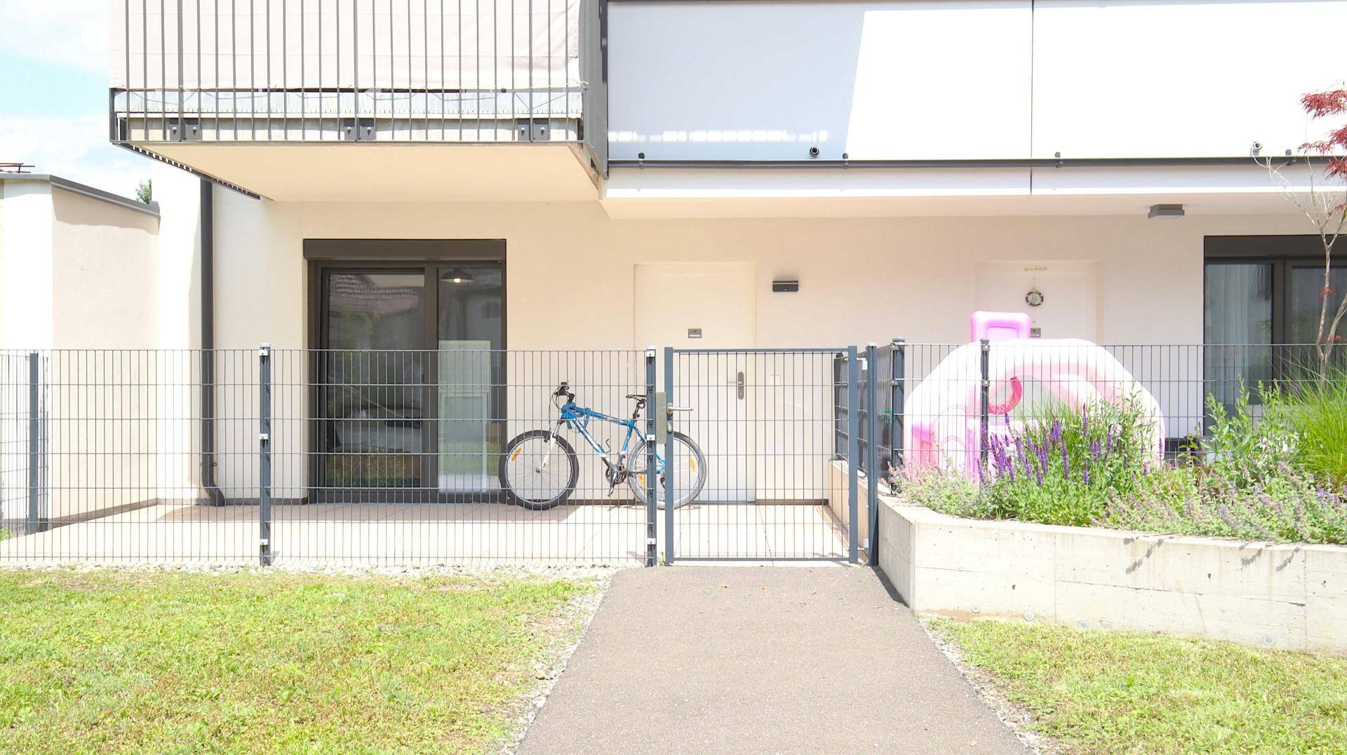 Außenansicht eines modernen Gebäudes mit Gartenbereich und Fahrradabstellplatz.