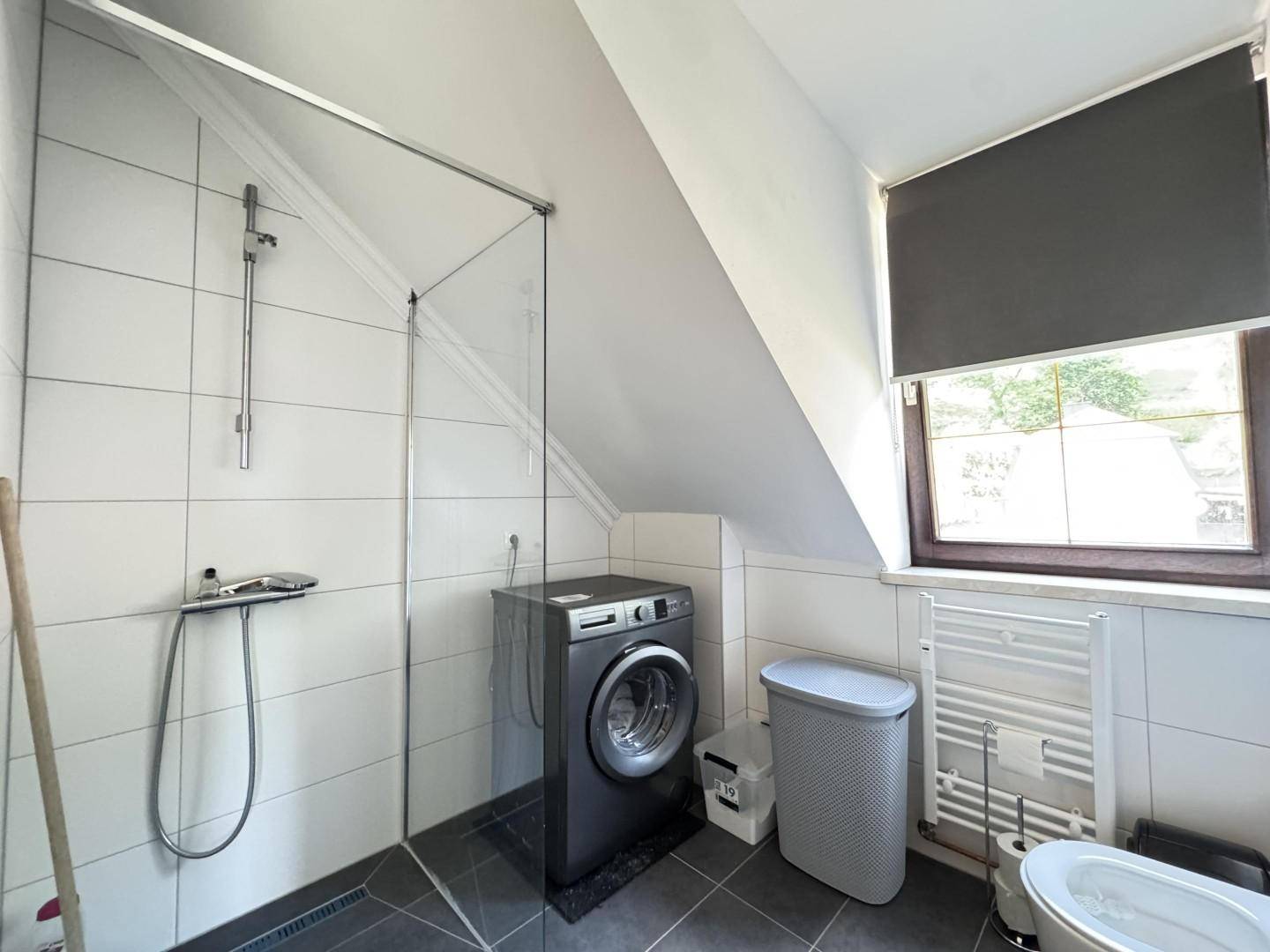Badezimmer mit begehbarer Dusche, Waschmaschine und Fenster unter der Dachschräge.