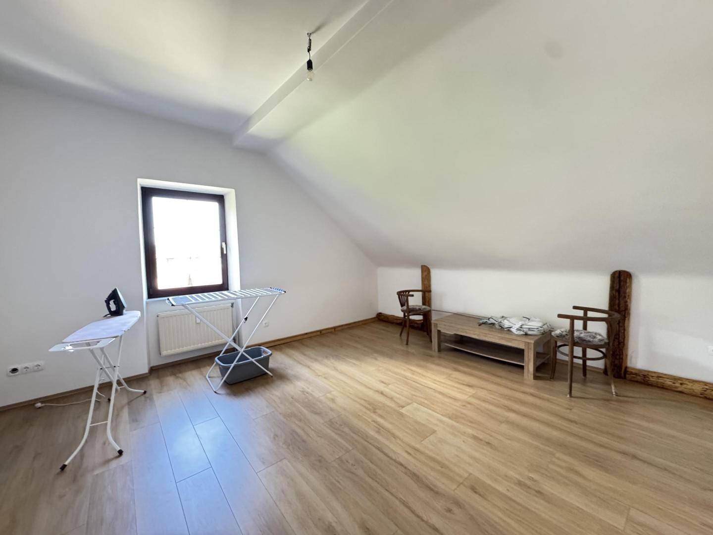 Heller Wohnraum mit Laminatboden, Fenster und schrägen Wänden, genutzt als Mehrzweckbereich.