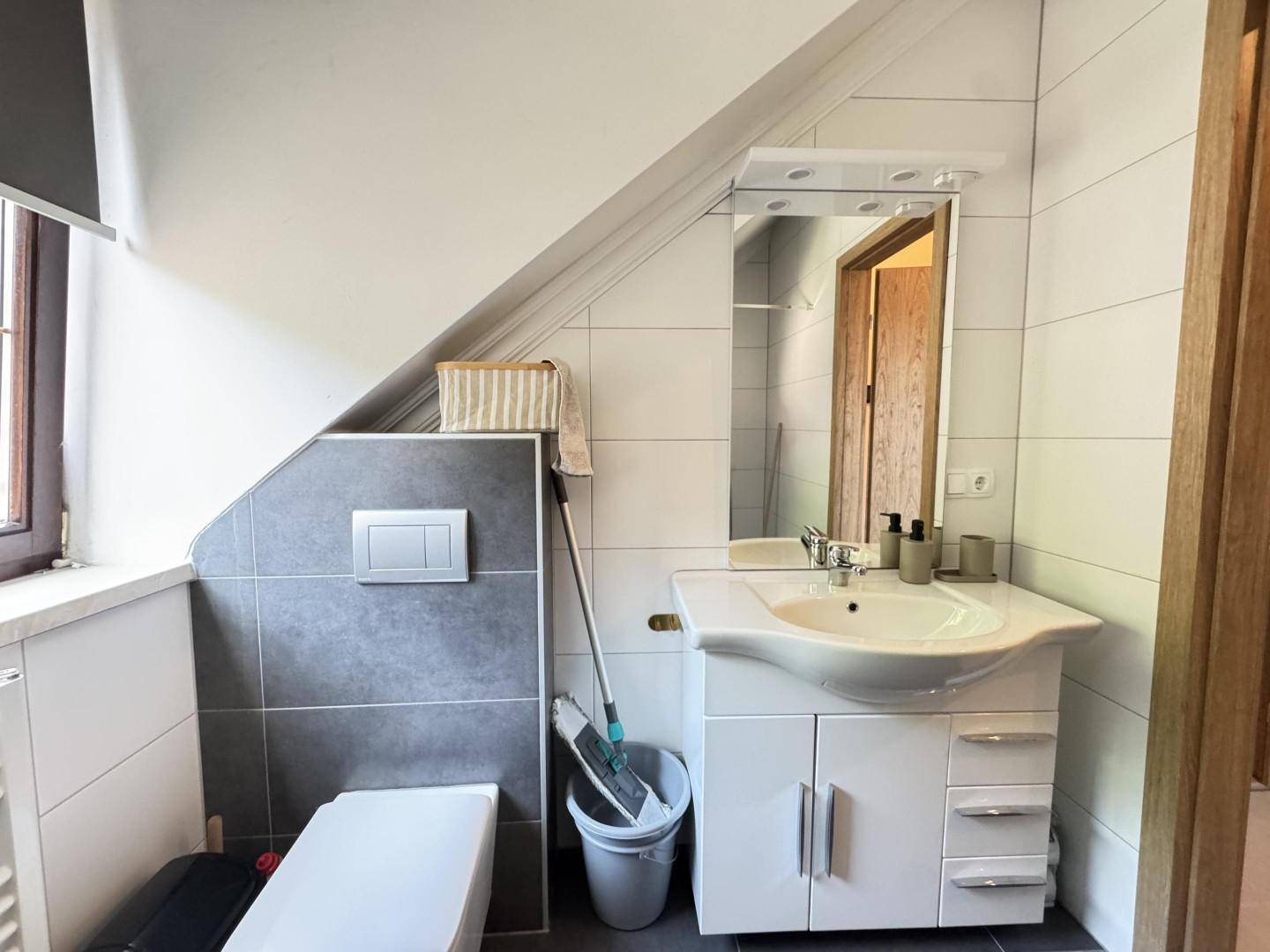 Modernes Badezimmer mit Waschtisch, WC und hellen Fliesen unter der Dachschräge.