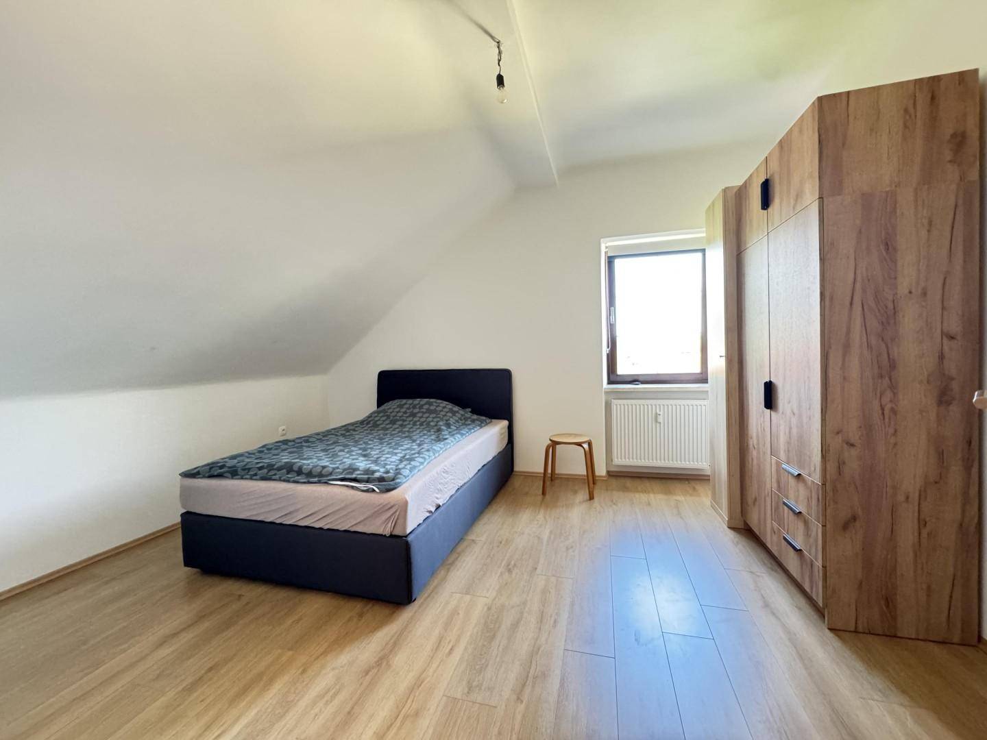 Schlafzimmer mit Einzelbett, Holzschrank und Fenster unter der Dachschräge.
