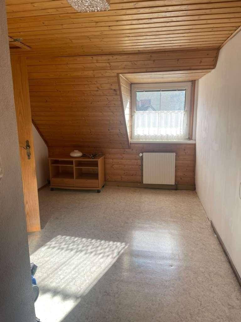 Heller Raum mit Holzverkleidung an Wänden und Decke, Dachschräge und einem Fenster mit Blick nach draußen.