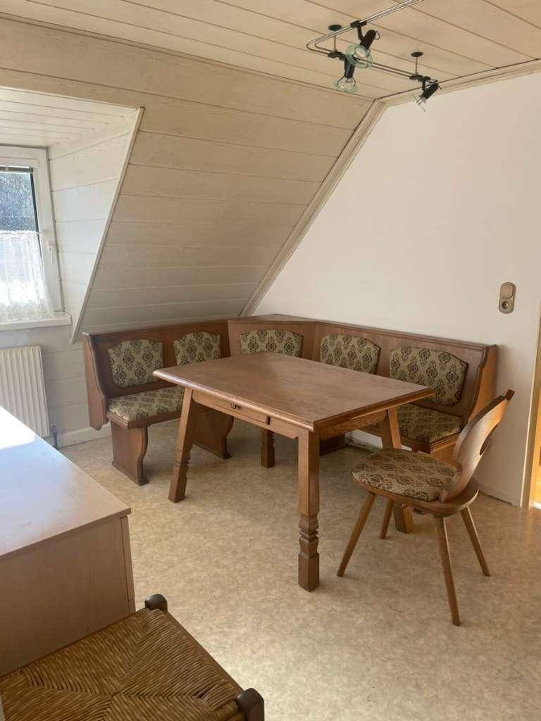 Gemütlicher Essbereich mit einer Eckbank und einem Holztisch unter einer Dachschräge, hell beleuchtet durch ein Fenster.