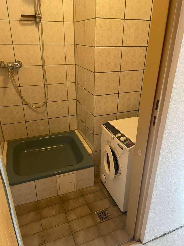 Kleines Badezimmer mit Duschbereich, Fliesen an Wänden und Boden sowie einer Waschmaschine.
