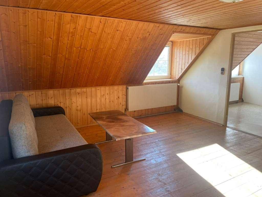 Gemütliches Wohnzimmer mit Holzverkleidung, Dachschräge, Sofa und einem Fenster, das Tageslicht hereinlässt.