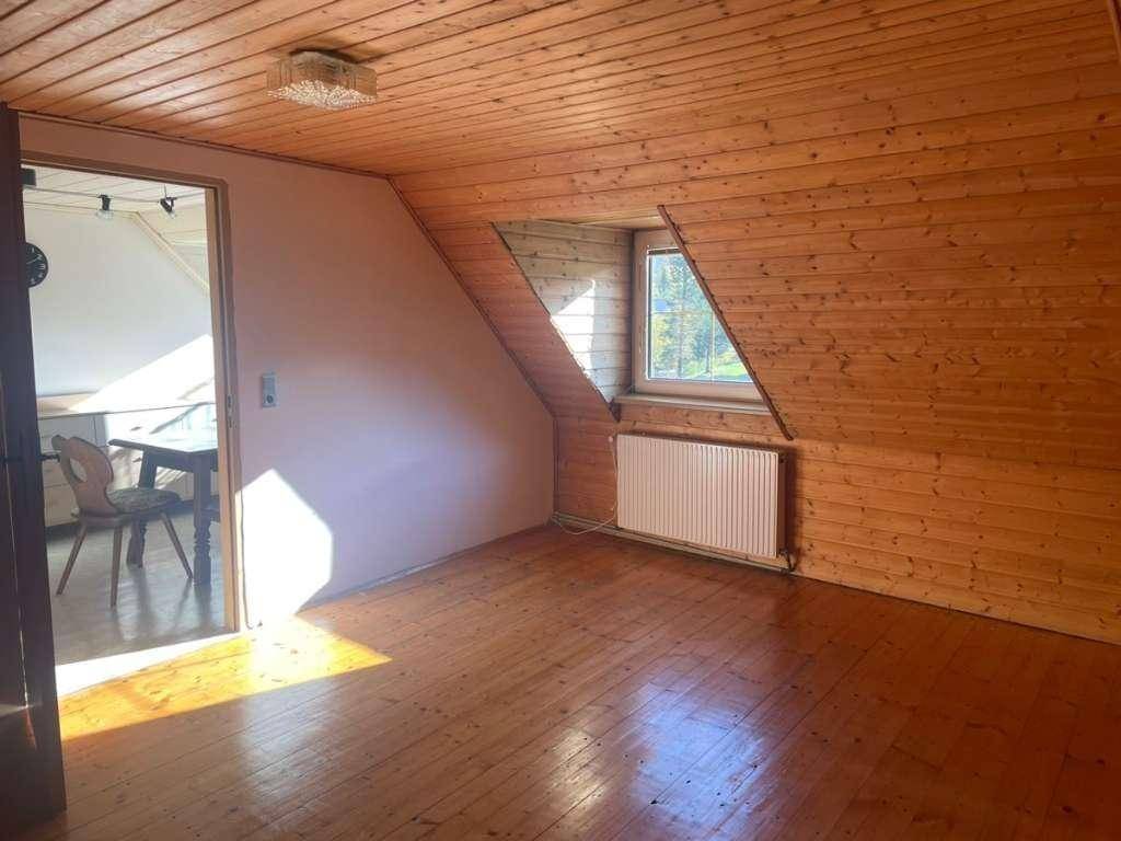 Schlafzimmer mit Holzboden und Holzverkleidung an Wänden und Decke, inklusive Dachschräge und Fenster.