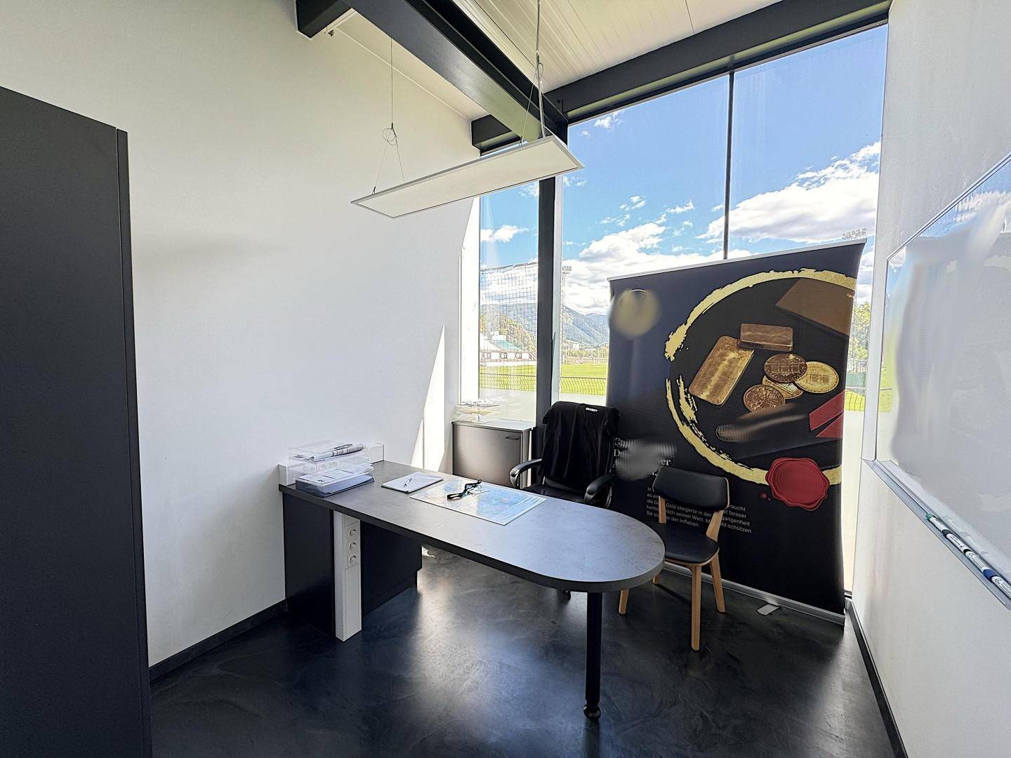 Helles Büro mit großflächigen Fenstern, einem modernen Schreibtisch und einem Werbebanner im Hintergrund.