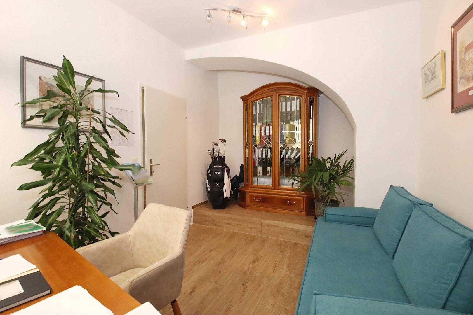 Bürobereich mit Sofa, Holzschrank und dekorativem Bogen, ausgestattet mit Laminatboden.