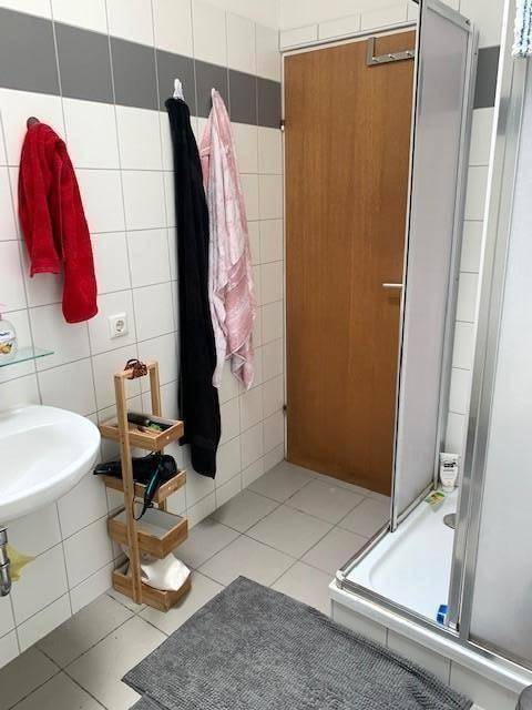 Badezimmer mit Duschkabine, Waschbecken und weißen Wandfliesen, praktisch gestaltet.