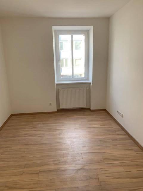 Helles Zimmer mit Laminatboden, weiß gestrichenen Wänden und einem großen Fenster.