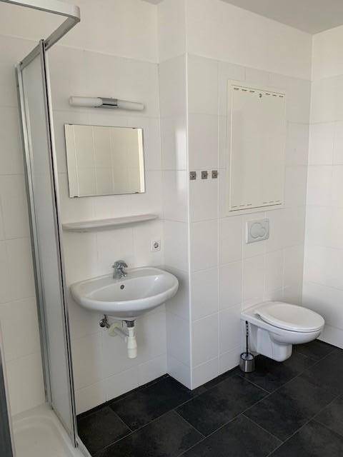 Funktionales Badezimmer mit Duschkabine, WC, Waschbecken und weißen Wandfliesen.