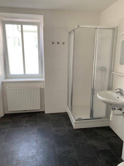 Modernes Badezimmer mit Dusche, Fenster und dunklen Fliesen auf dem Boden.