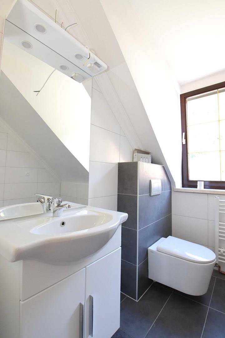 Modernes Badezimmer mit Waschbecken, wandhängendem WC, Spiegel und Dachfenster.