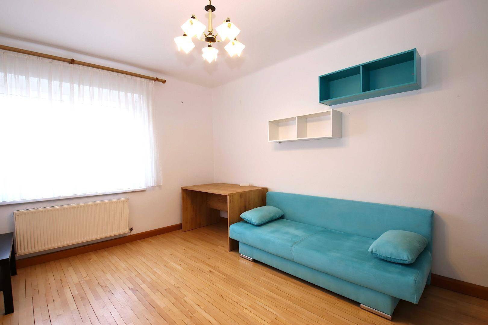 Helles Schlafzimmer mit Holzboden, türkisfarbenem Sofa und einem Schreibtisch am Fenster.
