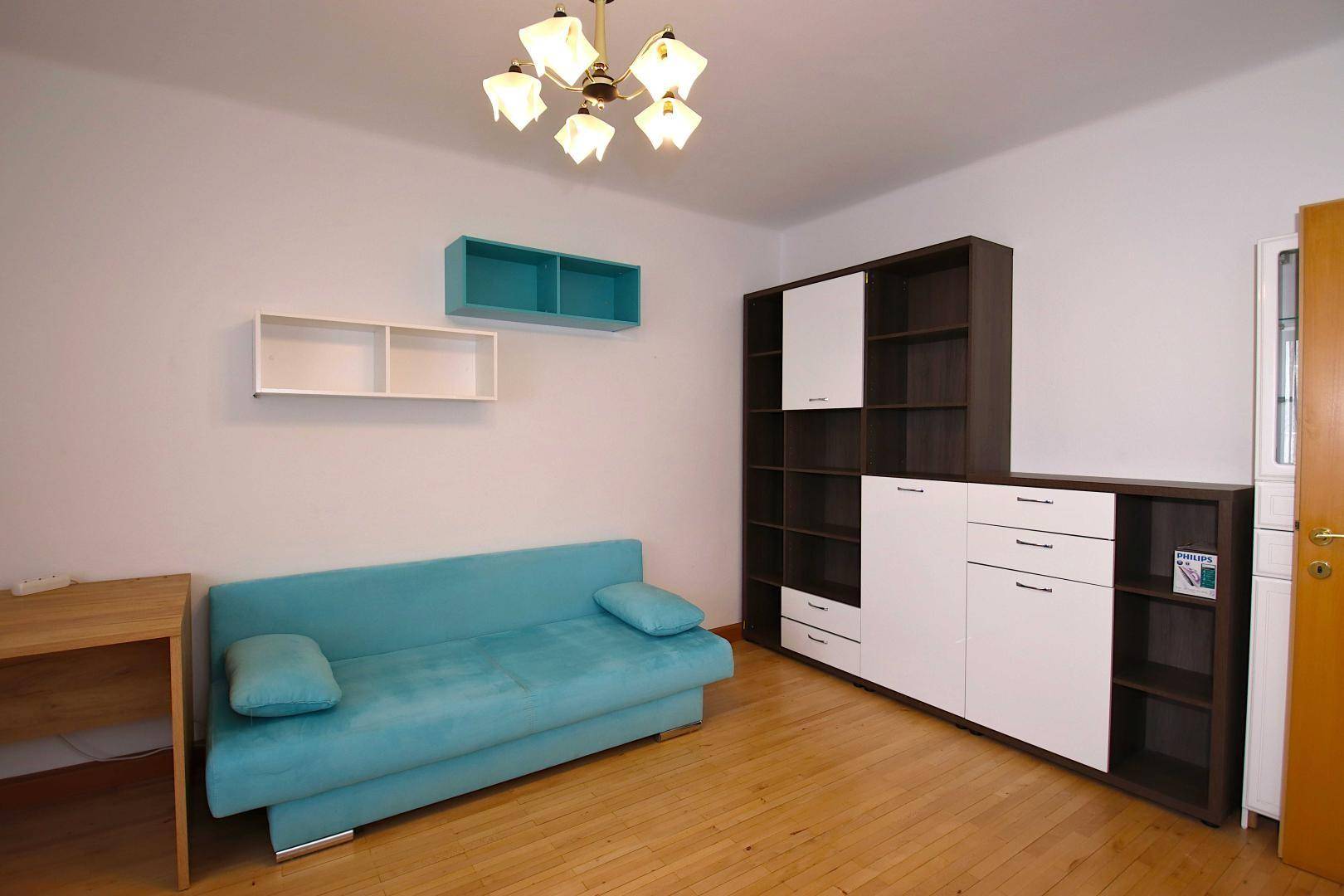 Schlafzimmer mit Holzboden, türkisfarbenem Sofa und großem Schrank mit offenen Regalen.