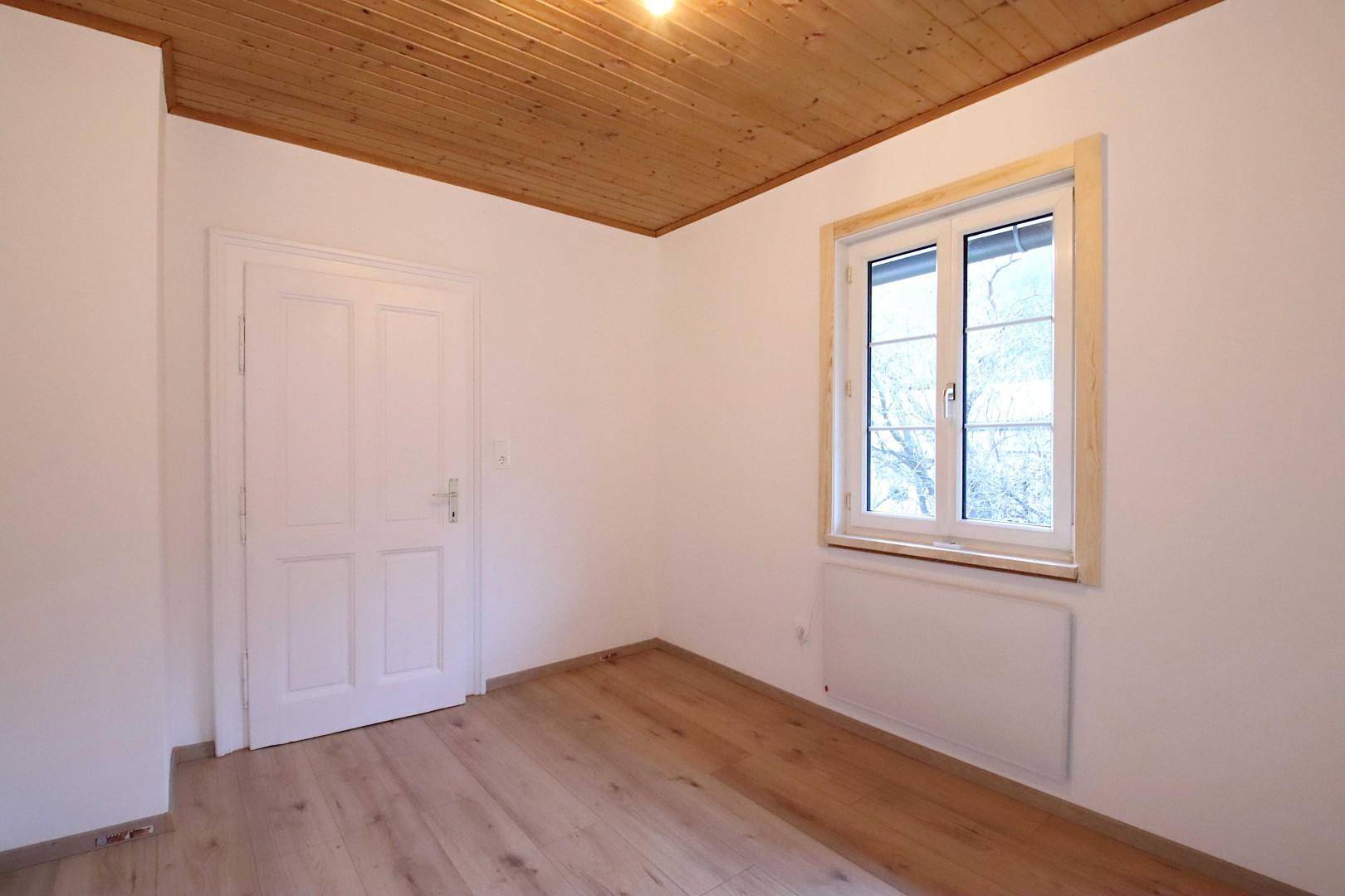 Helles Zimmer mit Holzboden, Fenster und Blick ins Grüne, ergänzt durch eine Holzdecke.