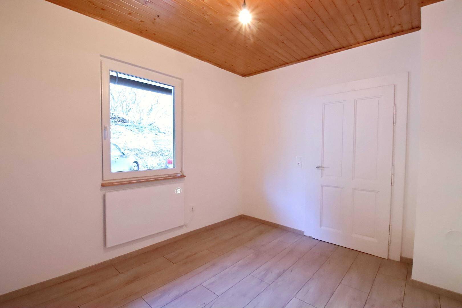 Freundliches Zimmer mit Holzboden, Fenster und Blick auf die umliegende Natur.