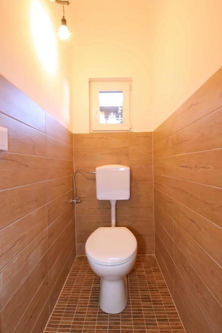 Kleines WC mit holzfarbenen Fliesen, Toilette und einem kleinen Fenster für Tageslicht.