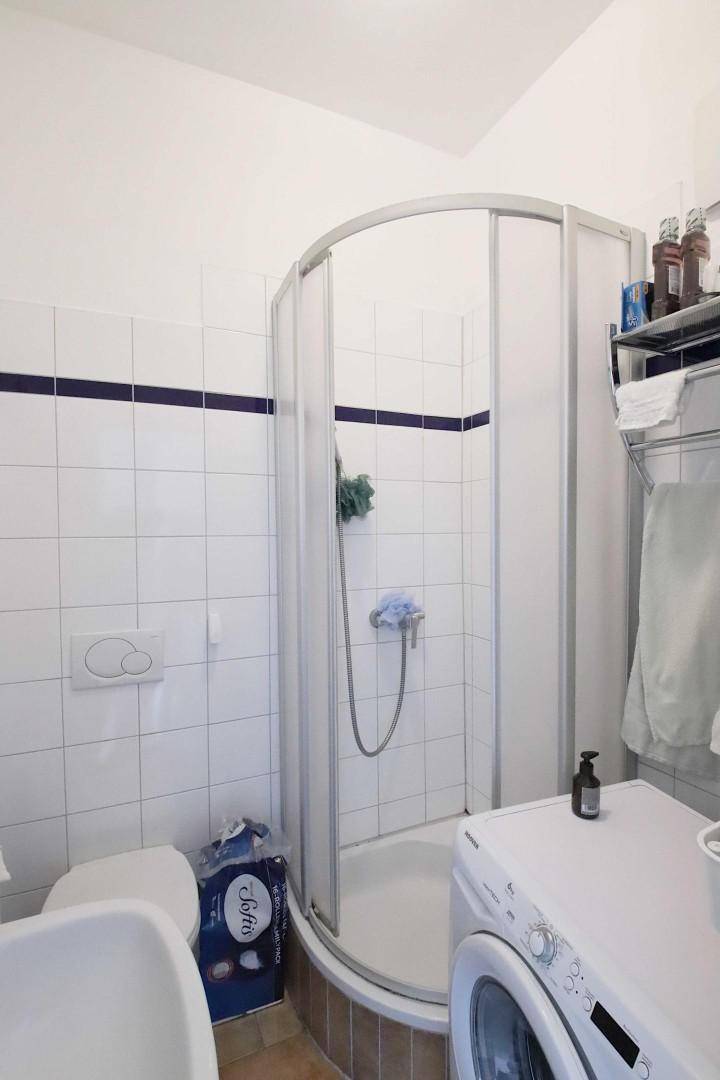 Badezimmer mit Duschkabine, Toilette und Waschmaschine, praktisch und hell gefliest.