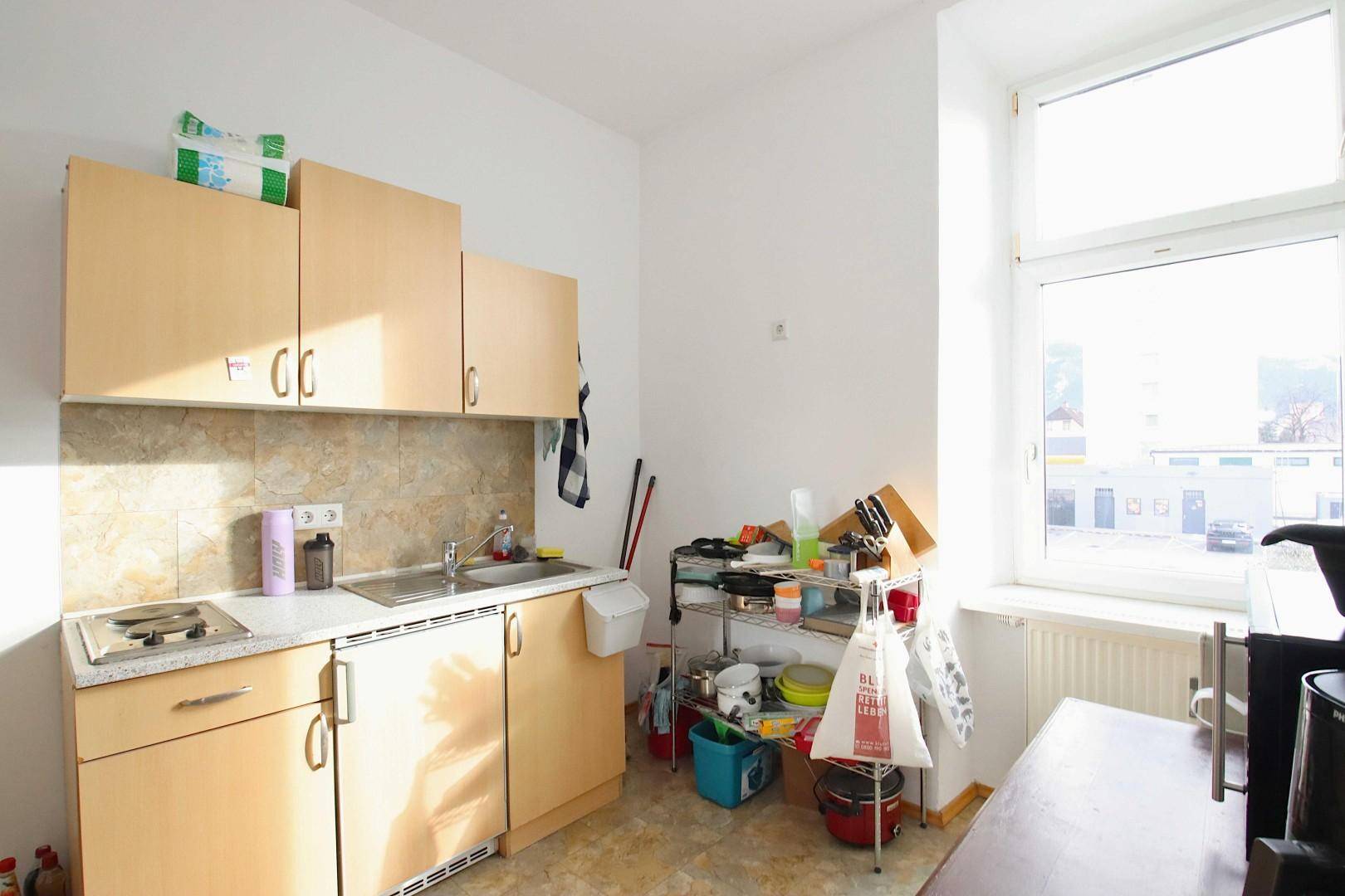 Funktionale Küche mit hellen Holzschränken, Spüle und Fenster, das den Raum erhellt.