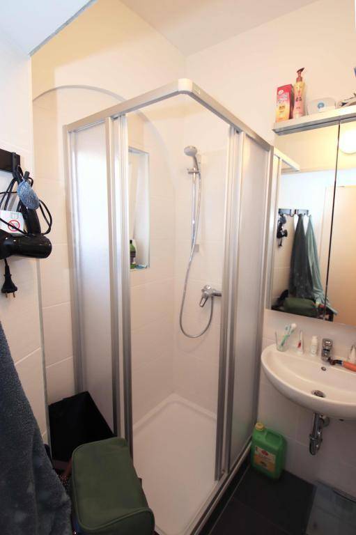 Badezimmer mit Duschkabine, Waschbecken und weißen Fliesen an den Wänden.