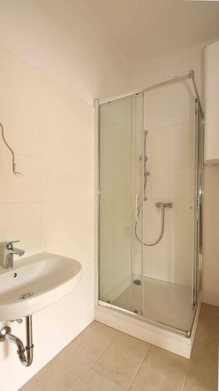 Funktionales Badezimmer mit Duschkabine, Waschbecken und hellen Fliesen an Wänden und Boden.