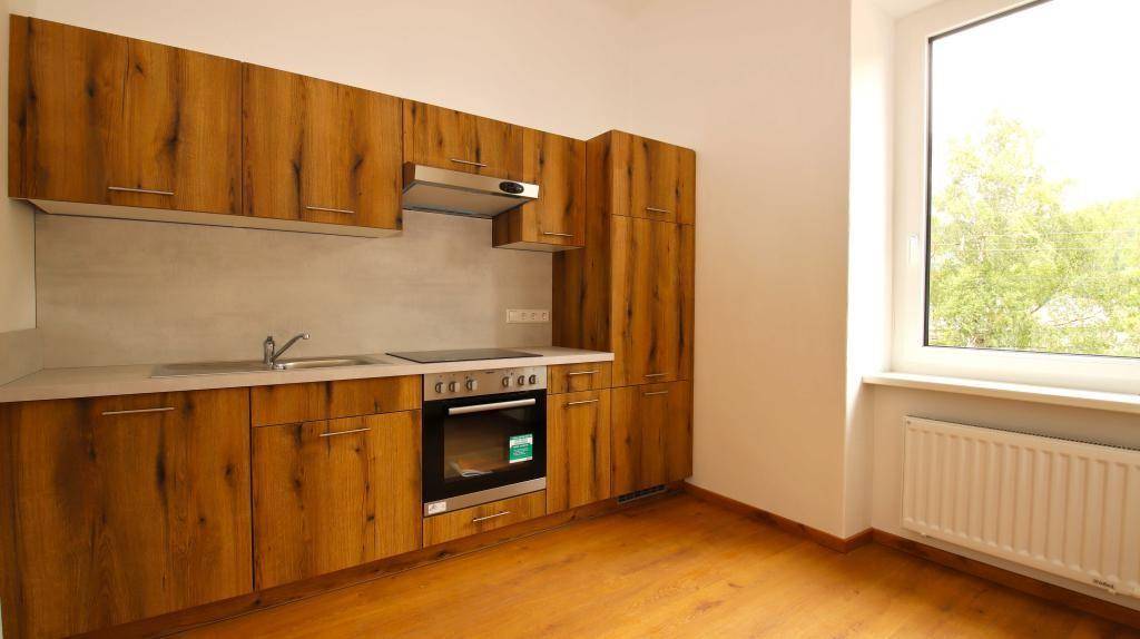Moderne Einbauküche mit Holzoptik-Fronten, integrierten Geräten und Fenster mit Grünblick.