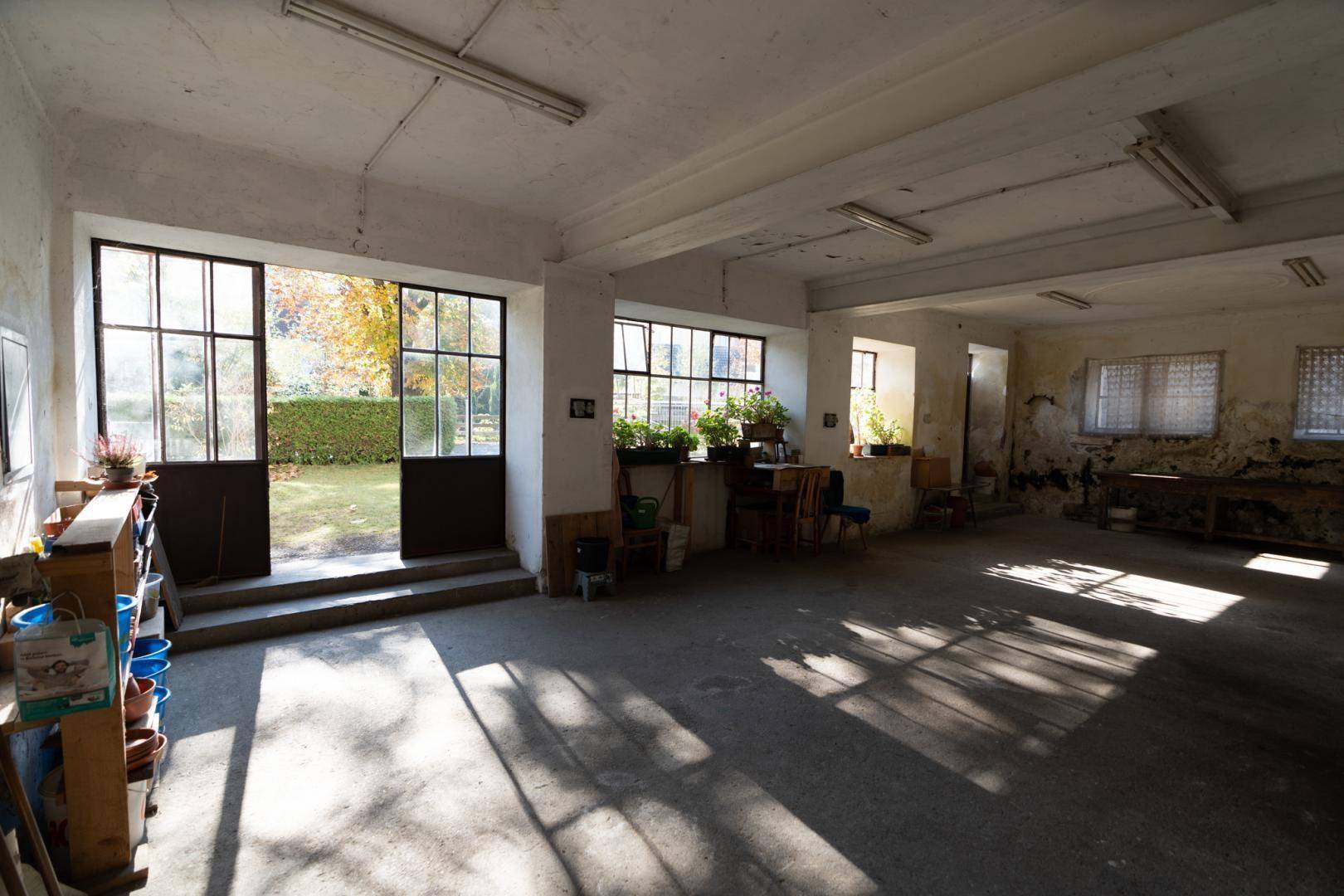 Heller Innenraum mit großen Fenstertüren zum Garten und Betonboden, durchflutet von Sonnenlicht.