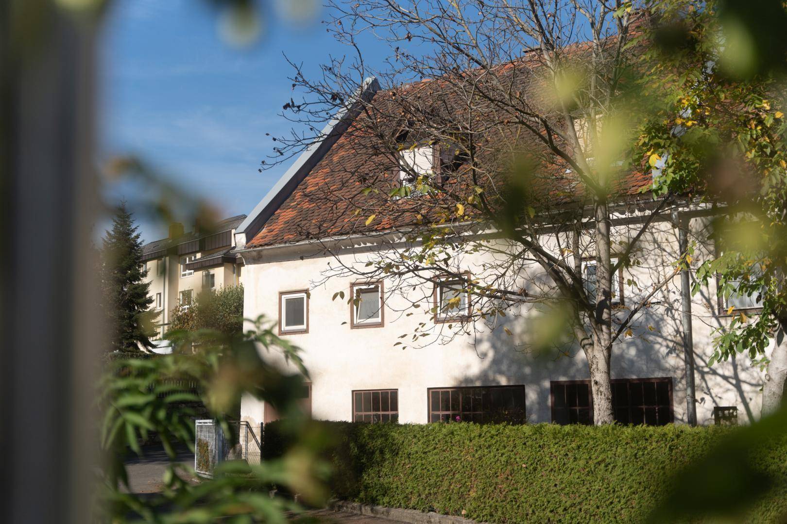 Älteres Gebäude mit Satteldach, umgeben von Bäumen und Hecken im warmen Herbstlicht.
