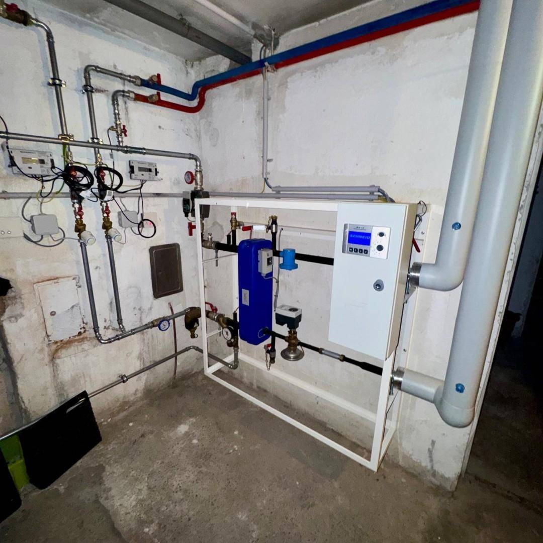 Technikraum im Keller mit Heizungsanlage und sichtbaren Rohrleitungen auf einem Betonboden.