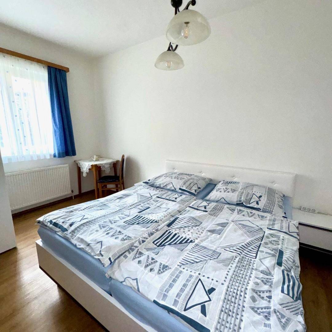 Gemütliches Schlafzimmer mit Doppelbett, Laminatboden und Fenster mit blauen Vorhängen für natürliche Beleuchtung.