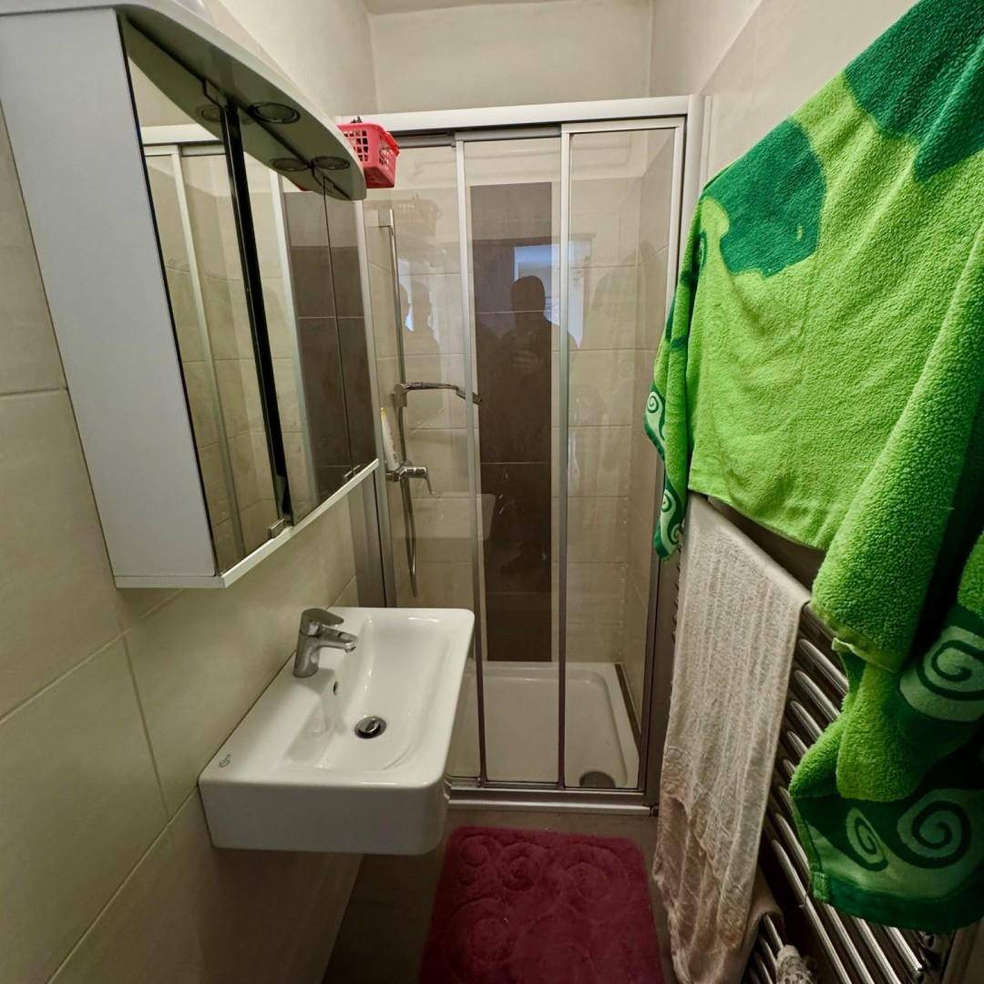 Kleines Badezimmer mit Duschkabine, Waschbecken und beheiztem Handtuchhalter für Komfort.