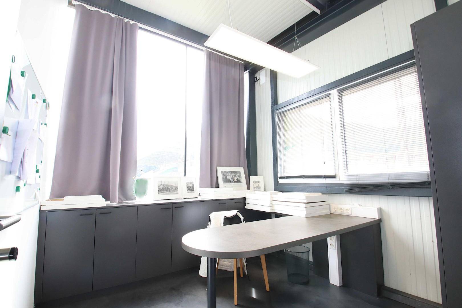 Modernes Büro mit großem Schreibtisch, dunklen Schränken und Vorhängen an den Fenstern.