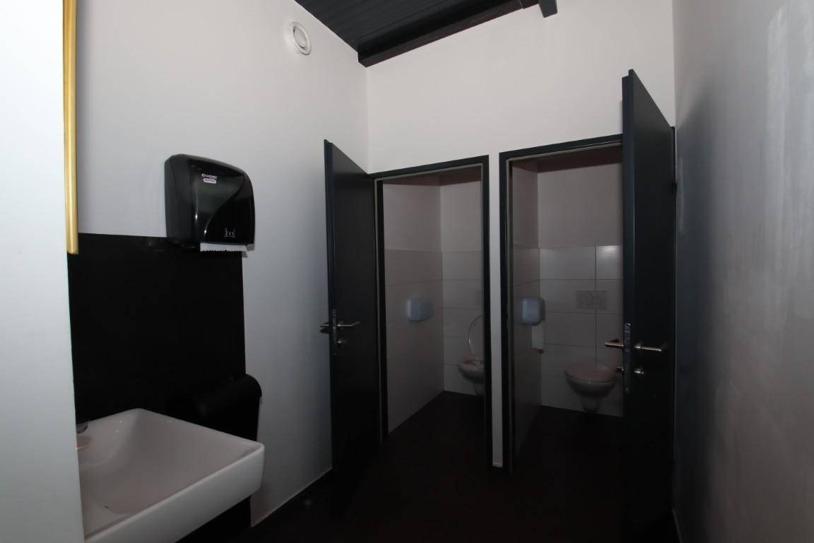 Waschbereich in der Toilette mit Waschbecken, Seifenspender und Zugang zu den Kabinen.